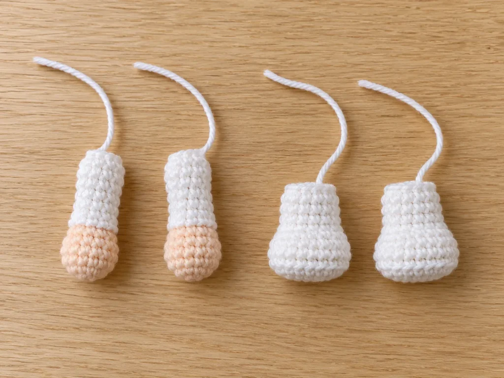 Two crochet nurse arms with skin-tone hands and white sleeves beside two small white legs, arranged before attachment.