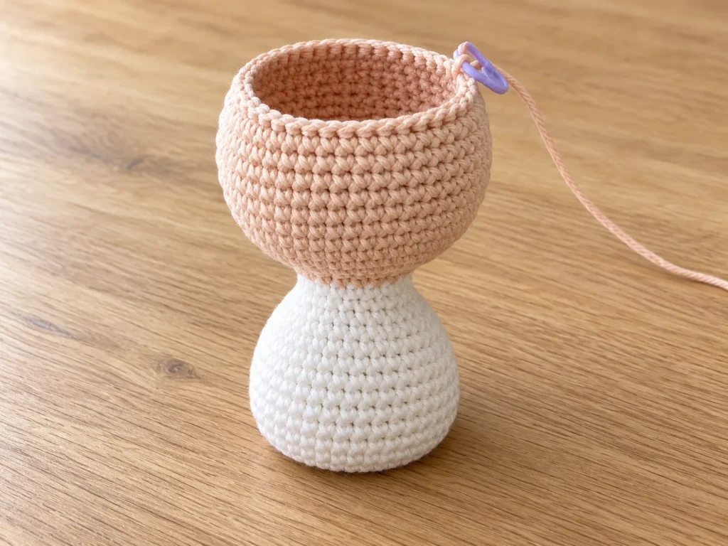 White crochet nurse body connected directly to an unfinished skin-tone head, with an open top and purple stitch marker.